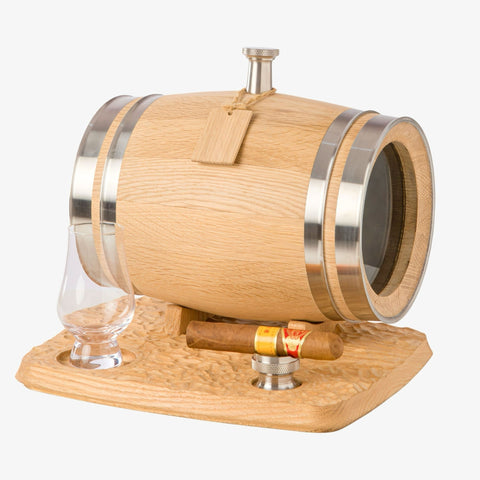 A 3L mini oak aging barrel with a glass window and steel bands, resting on a carved wooden base. The base also holds a whiskey glass and a cigar resting on a steel funnel.