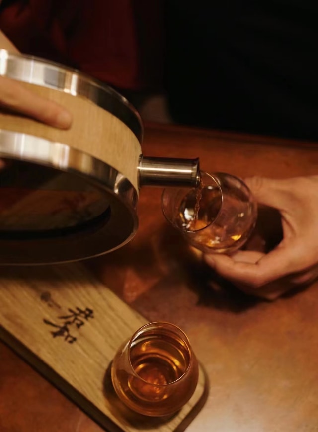 Pour the whiskey in the oak barrel decanter into a glass.