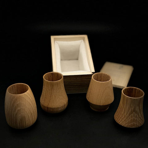 Four oak whiskey tumblers are in front of the wooden box.