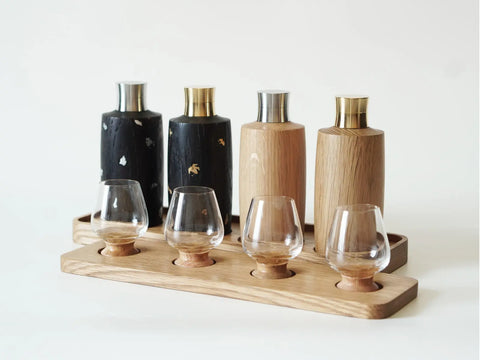 Four outdoor wine bottles and four small wine glasses are respectively placed on their corresponding oak bases.